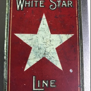 Puede incluir: Un letrero vintage rojo y blanco con el texto "White Star Line" y una estrella blanca en el centro.