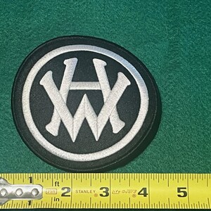 May include: A black and white embroidered patch with the letters "AW" in a circle. The patch is about 2 inches in diameter.