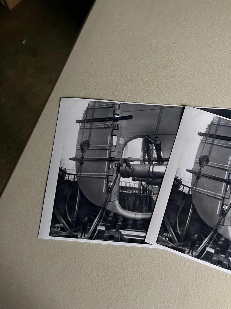 Pu&ograve; includere: Fotografia in bianco e nero di una grande struttura metallica in fase di assemblaggio da parte di due operai. La struttura &egrave; sollevata da una gru e sostenuta da travi in legno. La fotografia &egrave; scattata da un angolo basso, guardando verso l'alto la struttura.
