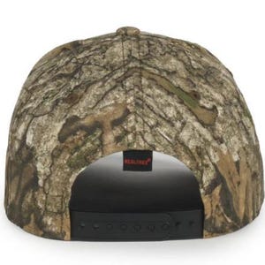 May include: A Realtree camouflage baseball cap. The cap has a brown, tan, and green pattern. The back of the cap has a black adjustable strap and a small black tag with the word "Realtree" in white.