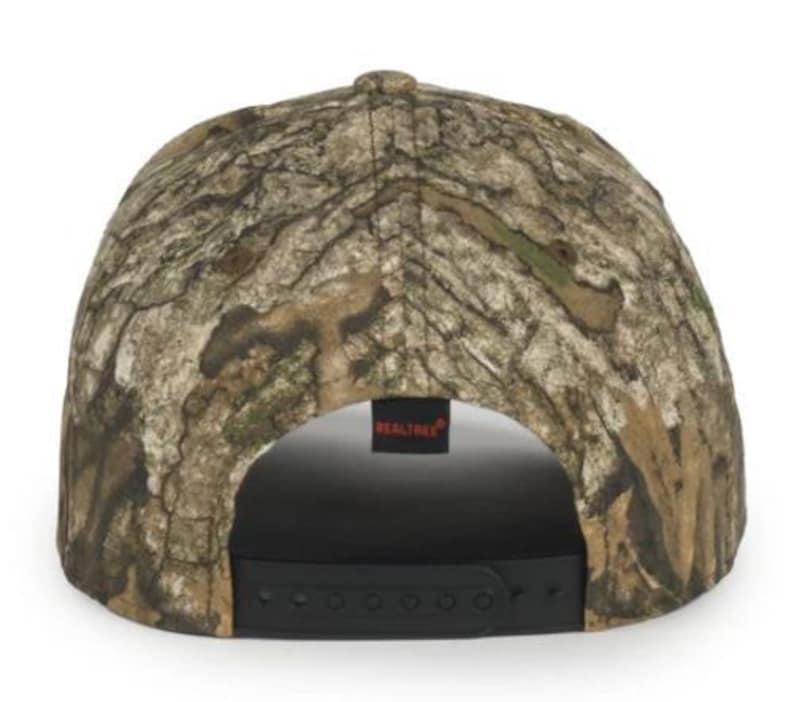 May include: A Realtree camouflage baseball cap. The cap has a brown, tan, and green pattern. The back of the cap has a black adjustable strap and a small black tag with the word "Realtree" in white.