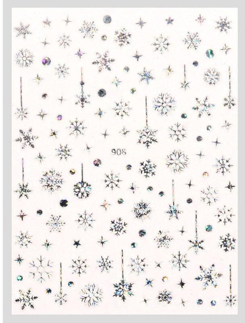 May include: A sheet of white nail stickers with a variety of silver snowflake designs. The sheet includes a number of different snowflake shapes and sizes, as well as some small stars and dots. The sheet is labeled "908".