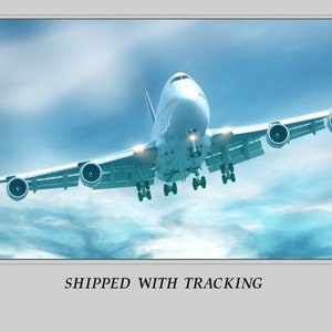 May include: A large white passenger airplane in flight against a blue sky with clouds. The plane has four engines and its landing gear is down. The text "SHIPPED WITH TRACKING" is at the bottom of the image.