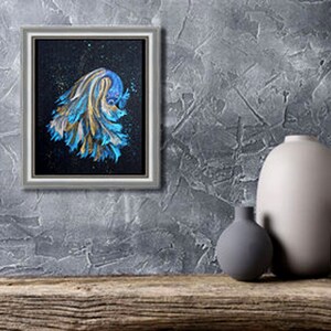 May include: A framed painting of a betta fish with blue and gold brushstrokes against a black background. The artwork is in a silver frame and is displayed on a textured gray wall. Decorative vases are on a wooden surface.