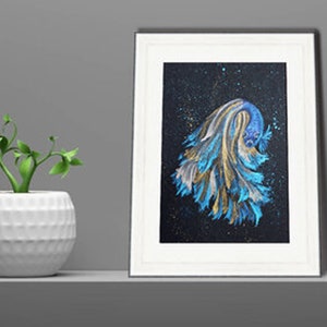 May include: Framed artwork featuring a vibrant betta fish illustration. The fish is depicted with flowing blue, gold, and white fins against a dark, speckled background. The artwork is in a white frame, displayed on a shelf with a small potted plant.