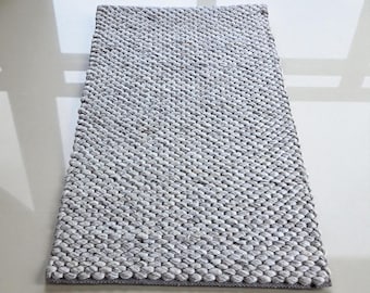 May include: A rectangular, gray woven rug with a textured, nubby surface. The rug is made of a light gray material and has a darker gray border. The rug is suitable for indoor use.