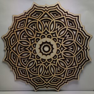 May include: A layered wooden mandala wall art piece. The design features concentric circles with intricate geometric patterns. The wood has a natural, light color with darker brown accents, creating a striking contrast. The artwork is circular and appears to be approximately 24 inches in diameter.