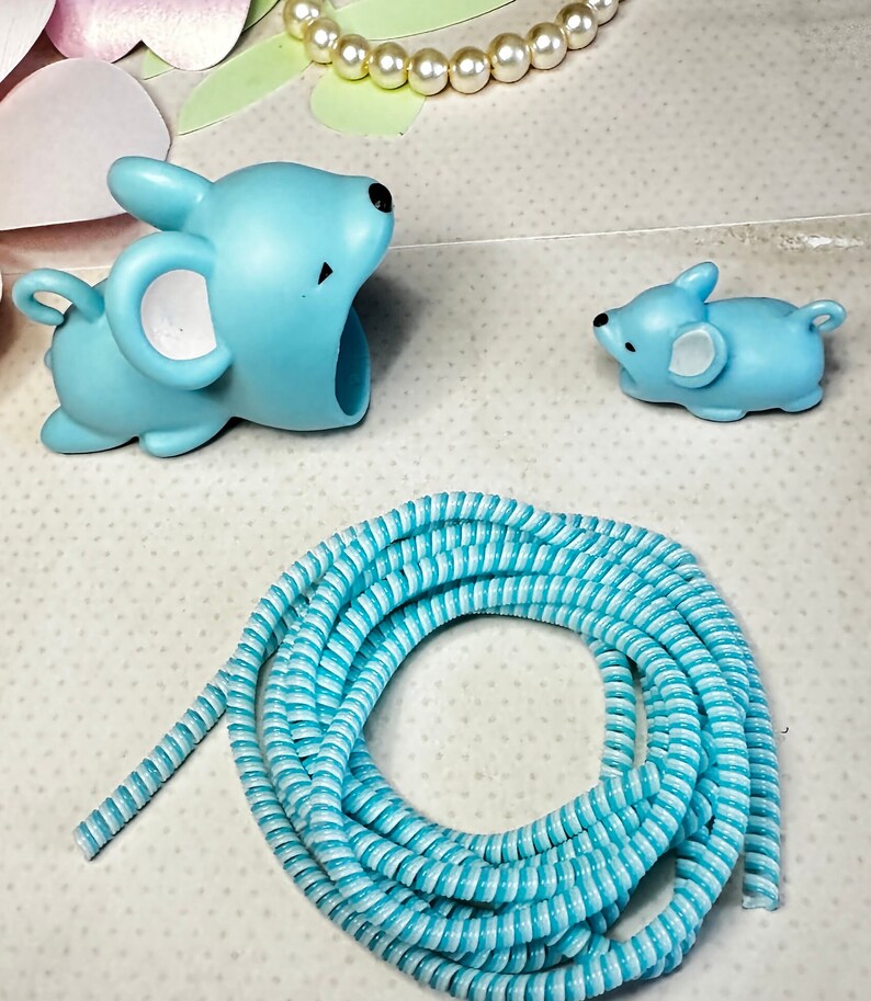 May include: A light blue mouse-shaped object with a large opening, a smaller mouse figurine, and a coiled blue and white striped cord. A pearl necklace and floral cutouts are in the background.