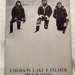 May include: A vintage concert program cover featuring three men in winter coats standing in the snow. The text "EMERSON LAKE & PALMER PROGRAMME" is printed in a serif font at the bottom of the cover.