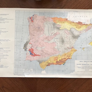 May include: A vintage map of Spain showing the seismic tectonic zones of the Iberian Peninsula and Balearic Islands. The map is printed on paper and has a grid pattern. The map is in shades of pink, yellow, red, and blue.
