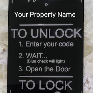May include: Black sign with silver lettering that reads "Welcome to Your Property Name".  The sign also has instructions on how to unlock and lock the door.  The instructions read "TO UNLOCK 1. Enter your code 2. WAIT... (Blue check will light) 3. Open the Door TO LOCK PRESS".