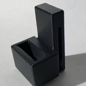 May include: A black plastic phone stand with a slot for a phone and a separate compartment for charging cables.
