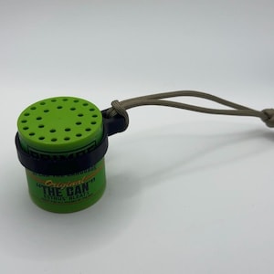 May include: A green cylindrical object with a black band and a series of small holes on top. The text "Original The Can" is visible. A tan cord is attached to the object.