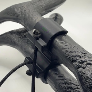 May include: Close-up of a black, textured object with a curved handle and a connecting bracket. A black cord is attached to the bracket. The object appears to be a part of a larger structure, possibly a handle or support.