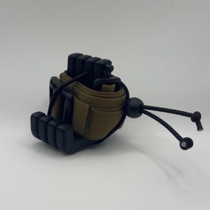 May include: A black and olive green tactical wrist cuff with a black adjustable cord and a black plastic clasp. The cuff is made of durable nylon material and features a secure design.