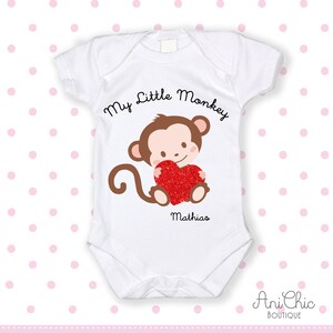 Puede incluir: Body de bebé blanco con un mono marrón que sostiene un corazón rojo brillante. El texto "My Little Monkey" está encima del mono, y el nombre "Mathias" debajo. El body es de Ani Chic Boutique.