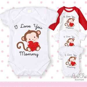 Puede incluir: Bodies y camisetas blancas para bebé con un diseño de mono sosteniendo un corazón rojo y el texto "I Love You Mommy". También se muestra una camiseta raglán roja y blanca con el mismo diseño.