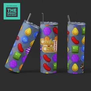 Puede incluir: Tres vasos de acero inoxidable con tapas y pajitas. Los vasos están decorados con un patrón de caramelos coloridos, incluyendo gominolas, piruletas y caramelos de goma. El vaso del medio tiene las palabras "Candy Crush Saga" impresas.
