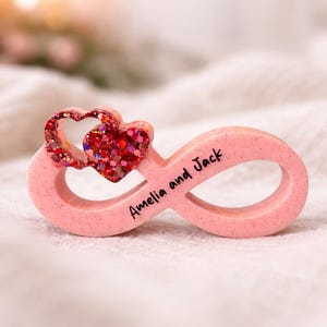 Könnte beinhalten: Ein rosa Unendlichkeitszeichen mit den Namen "Amelia and Jack" darauf geschrieben. Ein rotes Glitzerherz ist oben am Unendlichkeitszeichen befestigt. Das Unendlichkeitszeichen ist ein romantisches Geschenk.