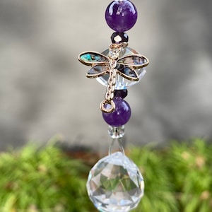 May include: A crystal suncatcher with a dragonfly charm and amethyst beads. The suncatcher has a clear crystal prism at the bottom.