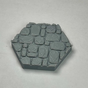 Peut inclure: Une tuile hexagonale en plastique gris avec une surface texturée qui ressemble à du pavé.