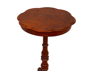 Op de afbeelding: Een kleine, ronde houten tafel met een gegolfde rand aan de bovenkant en een enkele, gedraaide voet. De tafel heeft drie poten die zijn versierd met een decoratief ontwerp.