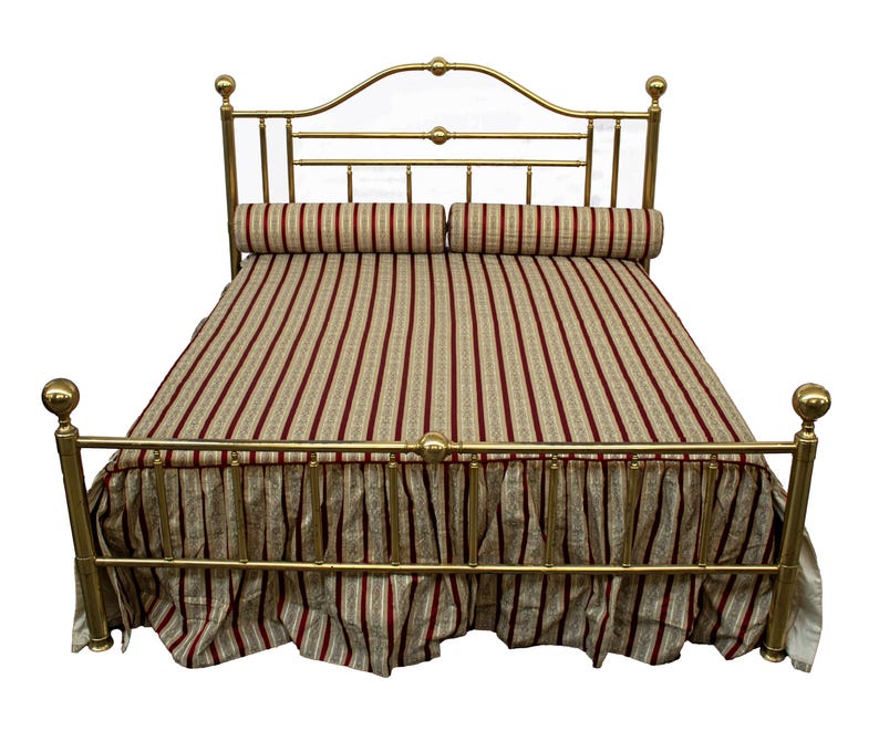 May include: A gold-colored metal bed frame with a curved headboard and footboard. The bed is made up with a striped comforter and matching bed skirt in shades of red, beige, and white. Two cylindrical pillows are placed on top.