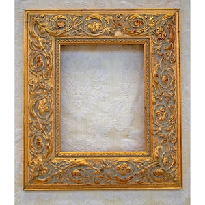 Könnte beinhalten: Ein verzierter Bilderrahmen in Gold mit einem detaillierten floralen Design. Der Rahmen ist aus Holz und hat eine leicht abgenutzte Oberfläche.