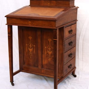 Op de afbeelding: Een vintage houten bureau met een neerlaatbare voorkant en vier laden. Het bureau heeft ingelegde ontwerpen en messing accenten. Het staat op wielen en heeft een lederen schrijf oppervlak.