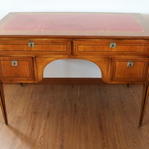 Può includere: Una scrivania in legno con un piano in pelle rossa e quattro cassetti. La scrivania ha un fronte curvo e quattro gambe.