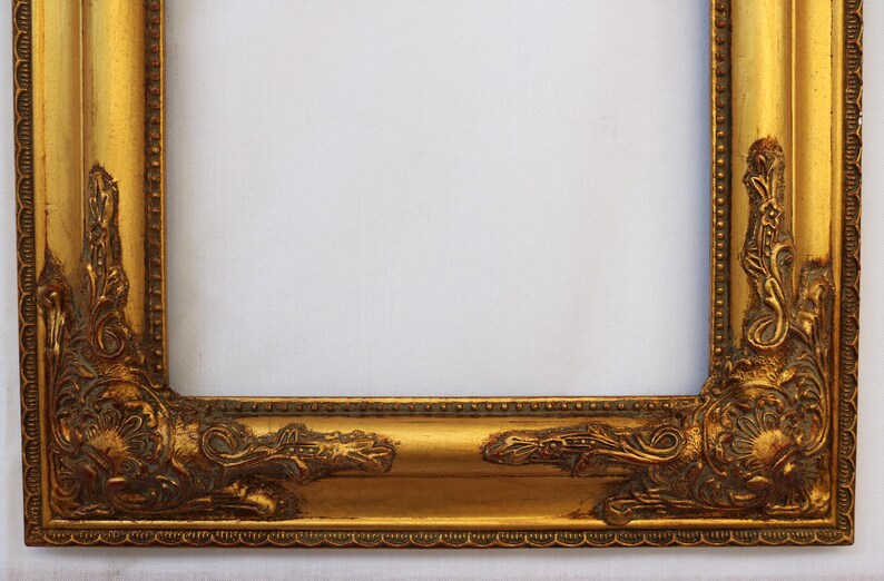 K&ouml;nnte beinhalten: Ein goldener Bilderrahmen mit verzierten Details an den R&auml;ndern. Der Rahmen ist aus Holz und hat eine Antik-Optik.
