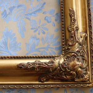 K&ouml;nnte beinhalten: Ein goldener Bilderrahmen mit verzierten Details und einem dekorativen Rand. Der Rahmen hat eine strukturierte Oberfl&auml;che und wirkt leicht gebraucht.