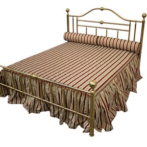May include: A brass bed frame with a striped comforter and a matching bed skirt. The comforter and skirt feature a pattern of red and beige vertical stripes. A cylindrical bolster pillow rests at the head of the bed.