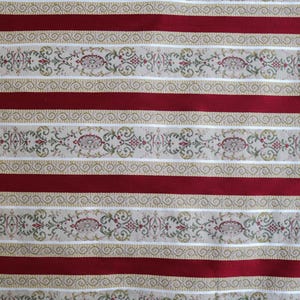 May include: Close-up of a fabric with a repeating pattern of alternating red stripes and decorative beige bands. The beige bands feature floral and scrollwork designs in green, red, and gold.