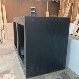 May include: A large, black, rectangular box with two openings on the front. The box is made of wood and has a rough, unfinished surface.