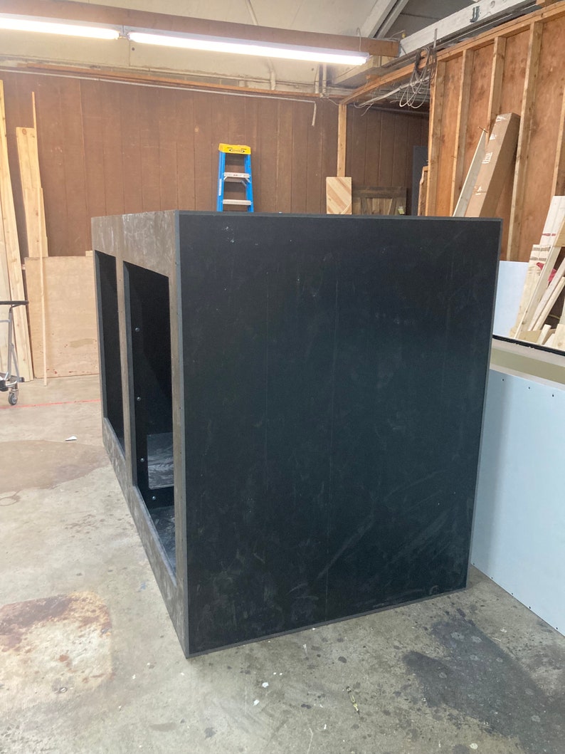 May include: A large, black, rectangular box with two openings on the front. The box is made of wood and has a rough, unfinished surface.