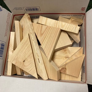 May include: A cardboard box filled with various sizes of unfinished wooden triangles. The box is open and the triangles are visible inside.