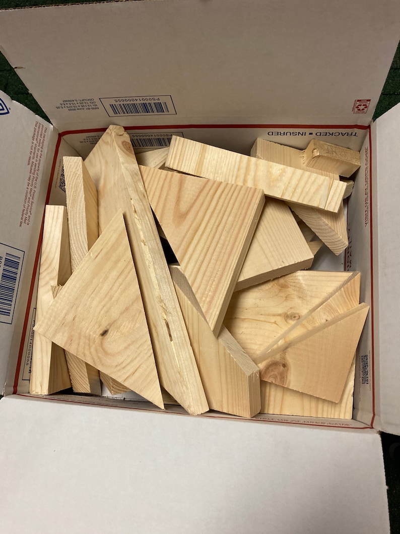 May include: A cardboard box filled with various sizes of unfinished wooden triangles. The box is open and the triangles are visible inside.