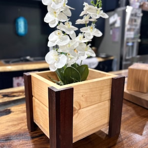 May include: A wooden planter box with dark brown trim, filled with white orchids. The planter is sitting on a wooden surface.