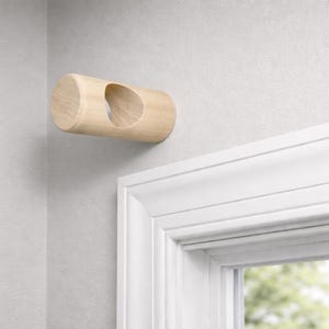 Könnte beinhalten: Ein helles, zylindrisches Wandhaken aus Holz mit einer ovalen Öffnung. Es ist an einer hellgrauen Wand in der Nähe eines weißen Türrahmens befestigt und hat ein minimalistisches Design.