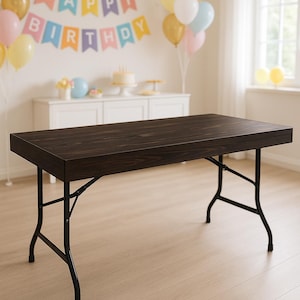 May include: A rectangular folding table with a dark brown wood grain top and black metal legs. The table features a thick wooden edge and a collapsible frame design with support braces on each side, providing a sturdy surface for various uses.