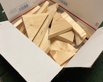 May include: A cardboard box filled with a variety of wooden triangles. The box is open and the triangles are visible inside. The box is sitting on a green surface.
