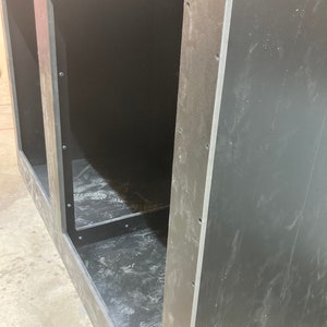 May include: A black wooden cabinet with two open compartments. The cabinet has a rough, unfinished look and is made of plywood.