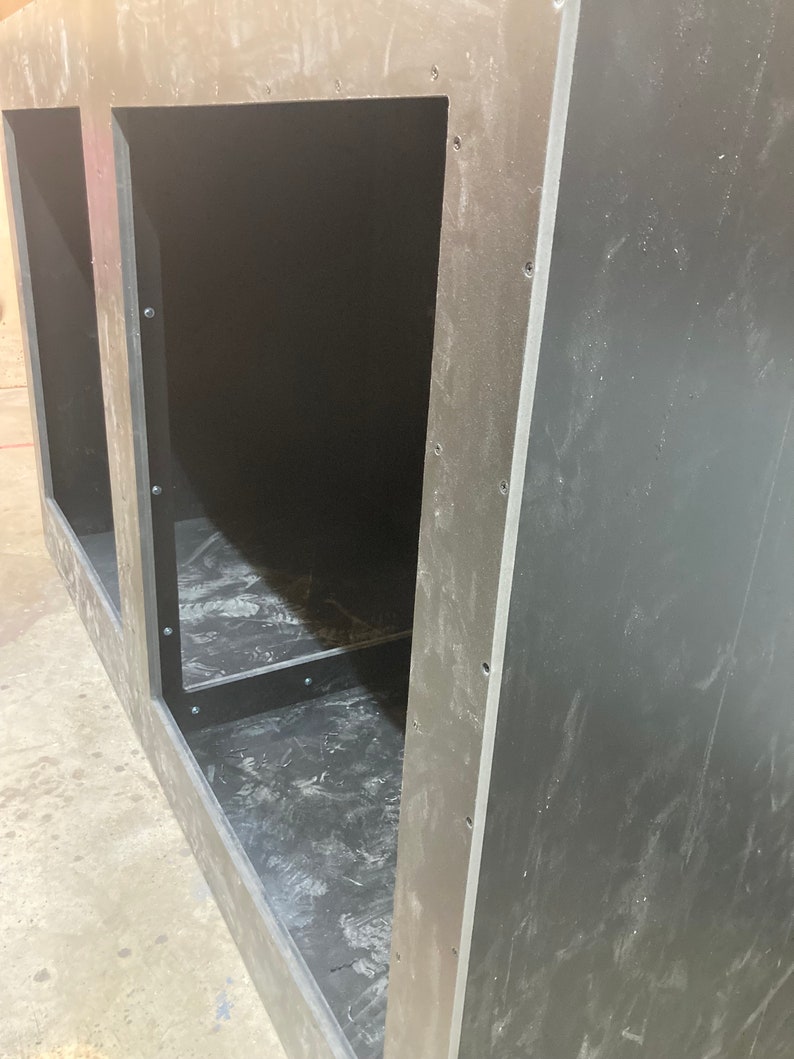 May include: A black wooden cabinet with two open compartments. The cabinet has a rough, unfinished look and is made of plywood.