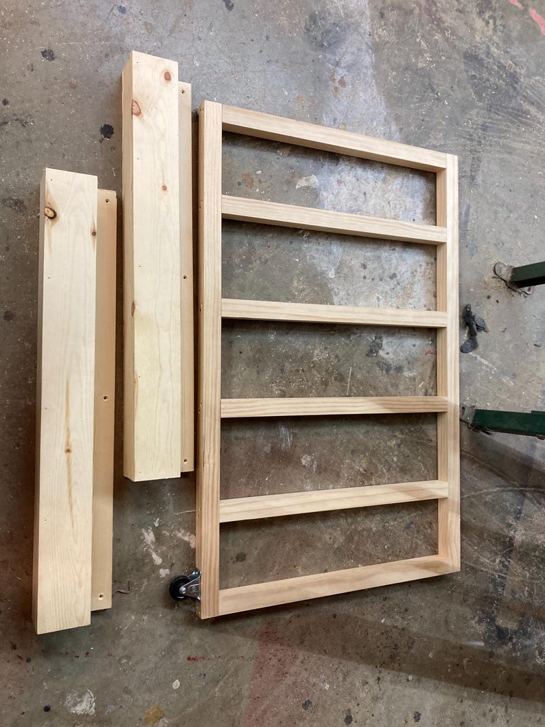K&ouml;nnte beinhalten: Unfertiger Holzrahmen mit horizontalen Lamellen und zwei vertikalen St&uuml;tzst&uuml;cken sowie zwei weiteren Holzst&uuml;cken. Der Rahmen hat unten ein Rad. Das Holz hat eine nat&uuml;rliche, helle Farbe.