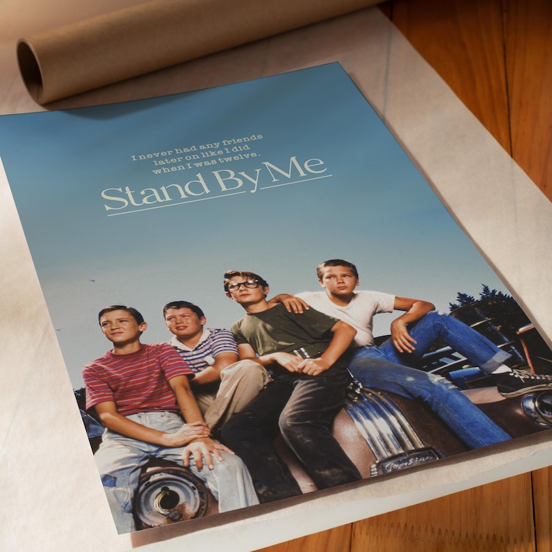 May include: A poster for the film "Stand By Me" featuring a group of young boys. The poster has a blue sky background with the film's title and a quote. The boys are sitting on a car.