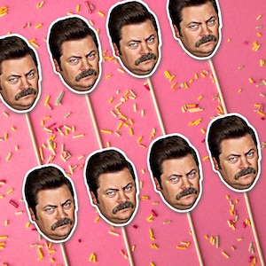 May include: A set of ten colourful cupcake toppers featuring a cartoon character with a moustache. The toppers are printed on cardstock and have a stick attached to the back.