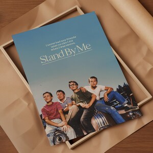 May include: A framed poster featuring the movie title "Stand By Me" with a group of young boys. The poster has a blue sky background and the quote "I never had any friends later on like I did when I was twelve."