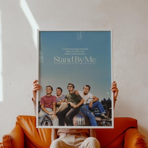 May include: A framed poster featuring the movie "Stand By Me." The poster has a blue background with the movie title and a quote. Four young boys are pictured in the bottom half of the poster. The frame is white.