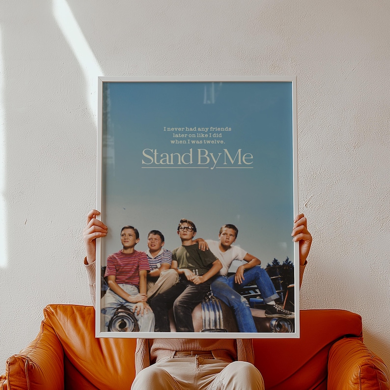 May include: A framed poster featuring the movie "Stand By Me." The poster has a blue background with the movie title and a quote. Four young boys are pictured in the bottom half of the poster. The frame is white.